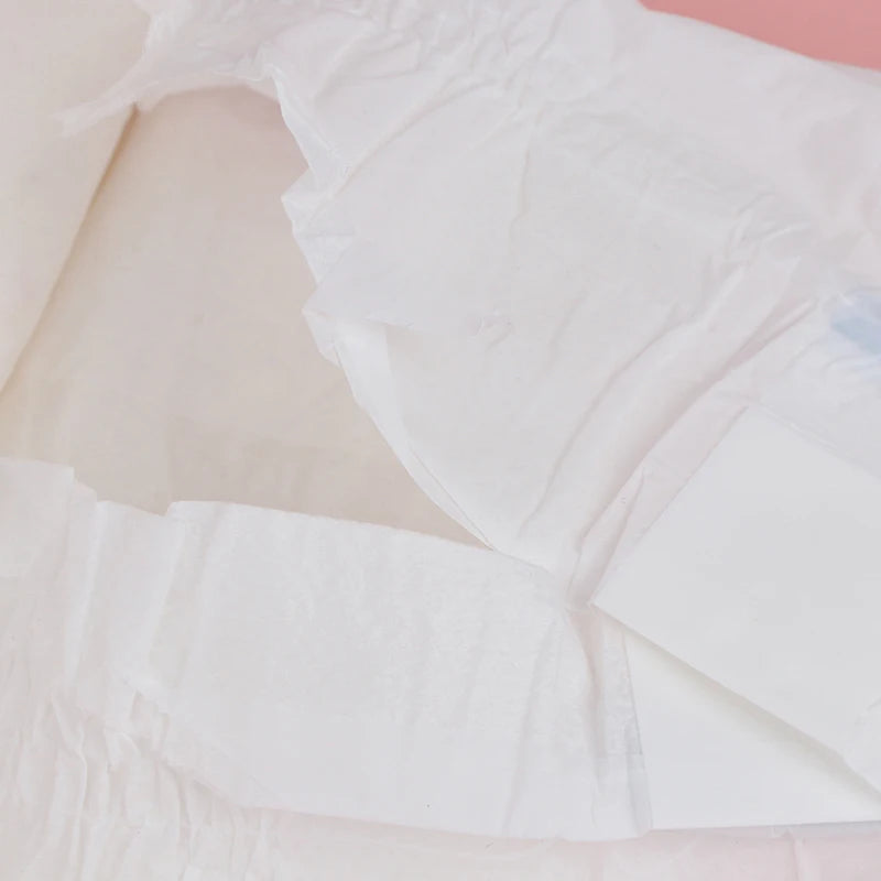 Detalhe da fralda Reborn branca com reforço absorvente, em fundo rosa claro.