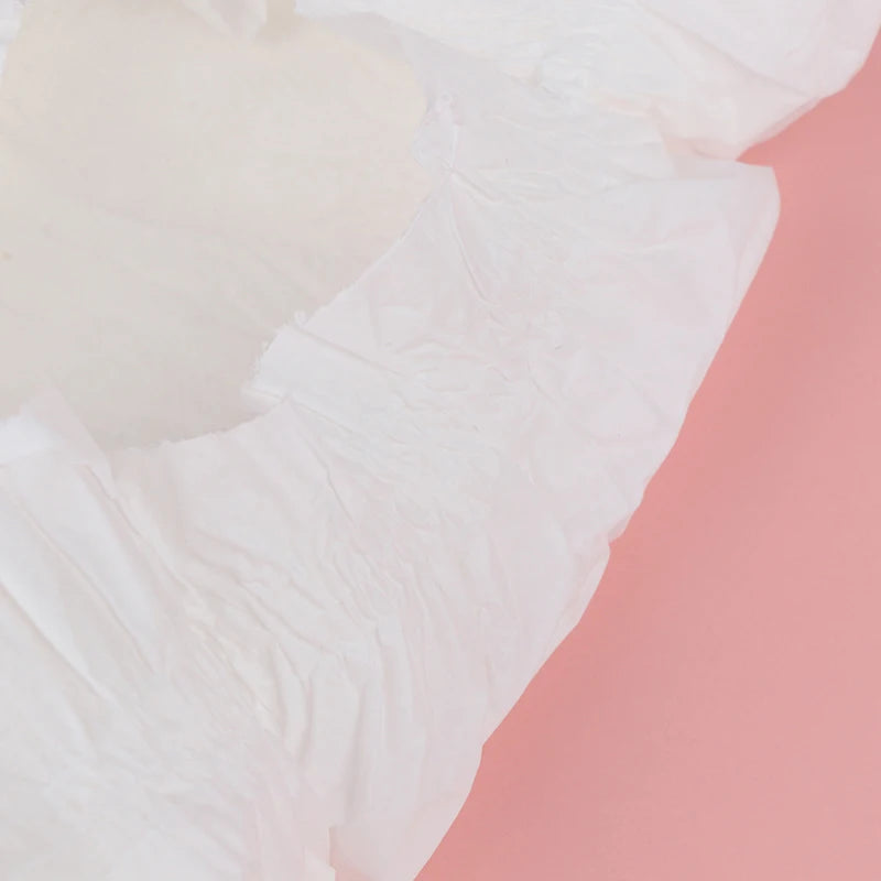 Close-up de fralda Reborn aberta, mostrando textura branca da fralda com fundo rosa.